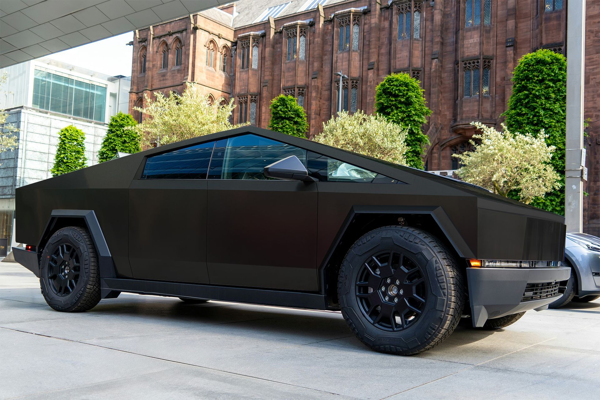 Black Tesla Cybertruck parked on a city street, with a brick building in the background.