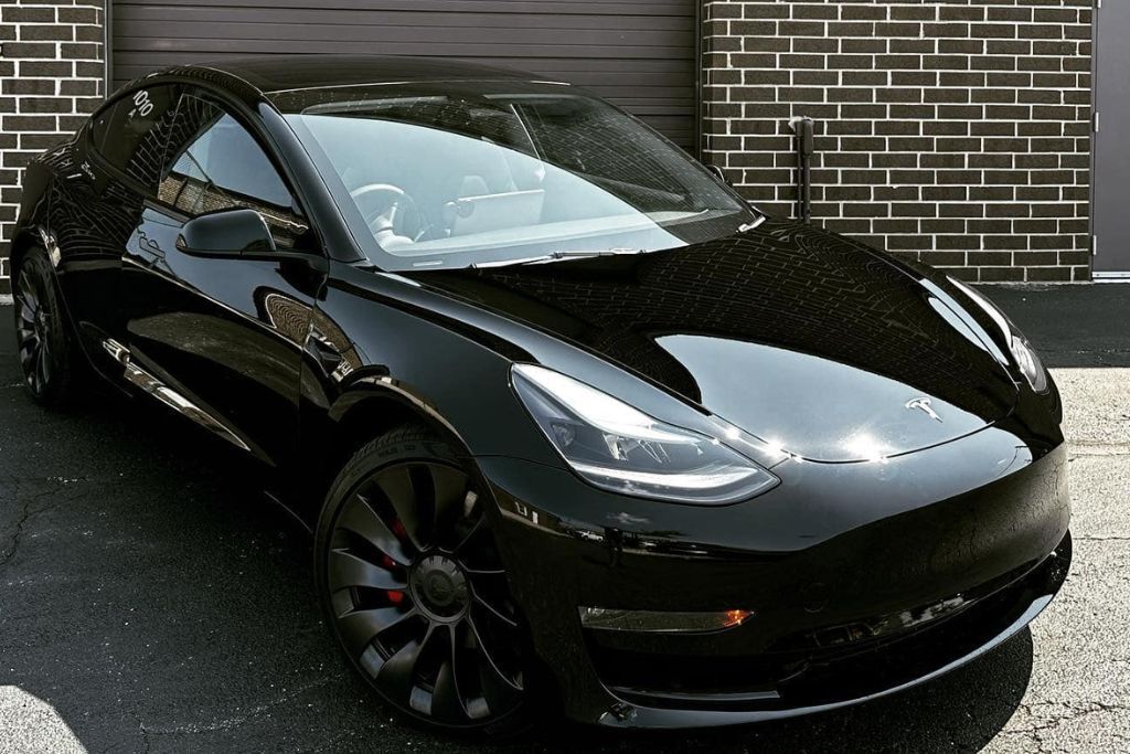 A black Tesla with a high-gloss finish parked against a brick wall, showcasing the pristine shine and protection provided by paint protection film.