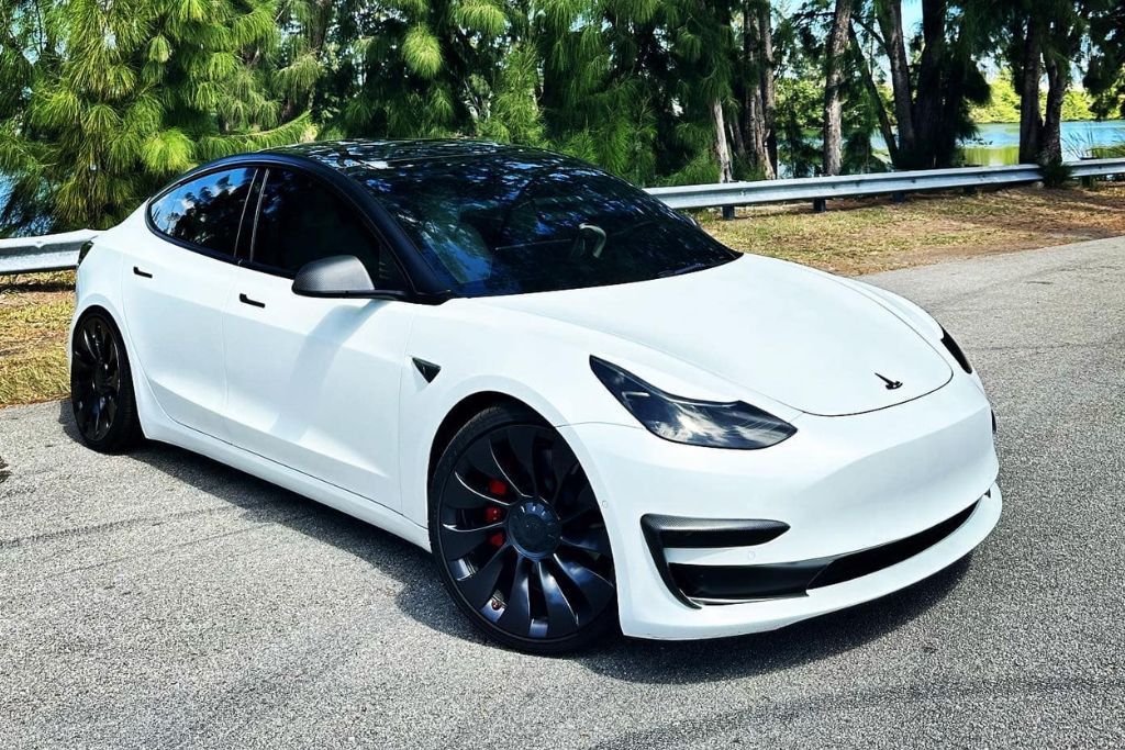 A Tesla Model 3 with a two-tone wrap featuring a matte white body contrasted by a glossy black roof, side mirrors, and wheel accents. The wrap adds a sleek and modern aesthetic to the car's design.
