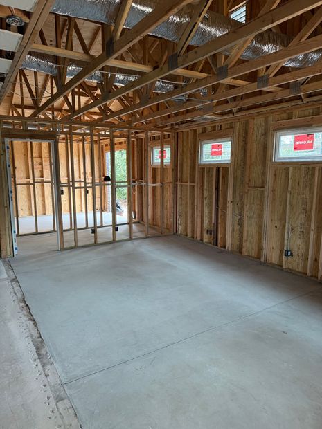 Unfinished room under construction with exposed wooden framing, trusses, and a concrete floor.