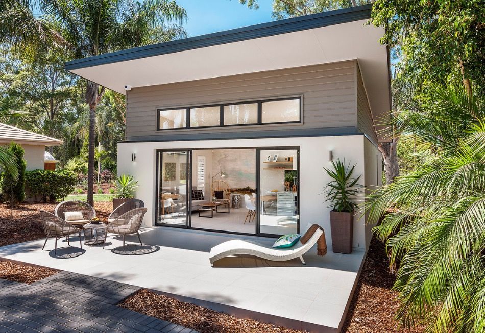 Modern house patio with sliding glass doors, outdoor seating, and lounge chairs surrounded by trees