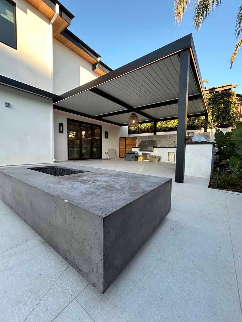 Modern patio with concrete seating, black pergola, and white house exterior.
