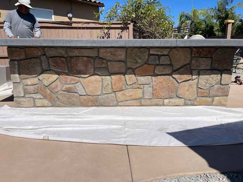 Stone outdoor bar with tan top and white tarp covering the ground, worker partially visible on the left