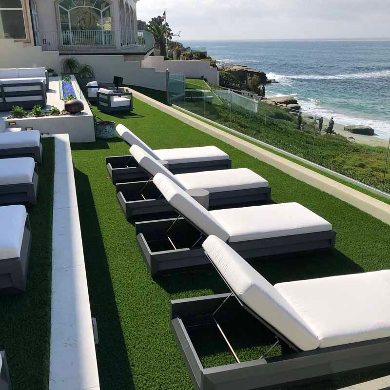 Modern seaside patio with white loungers and green turf overlooking the ocean