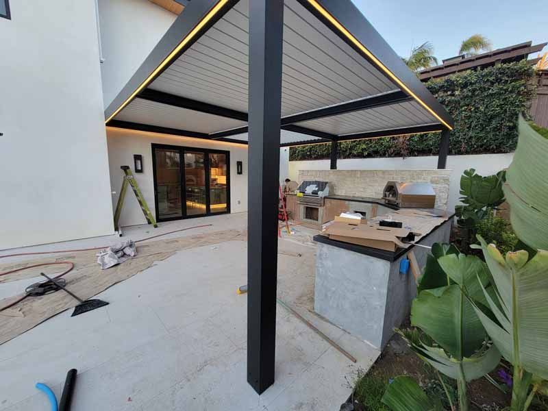 Modern outdoor patio with black pergola, built-in grill, concrete counters, and sliding glass doors