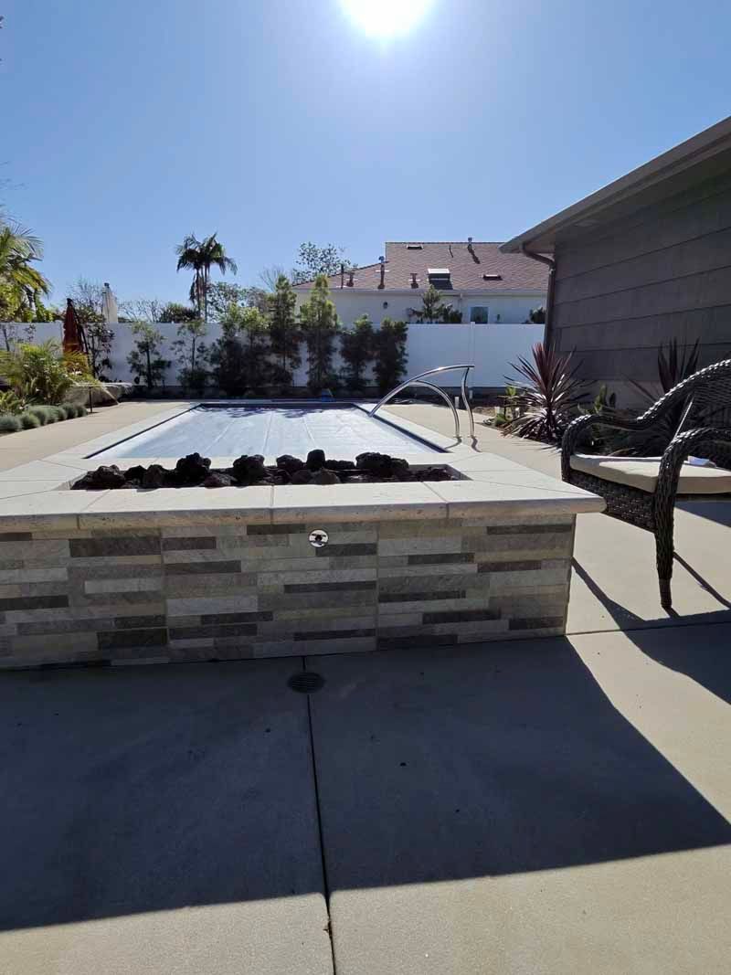 Backyard patio with a raised stone planter and benches under a bright sunny sky