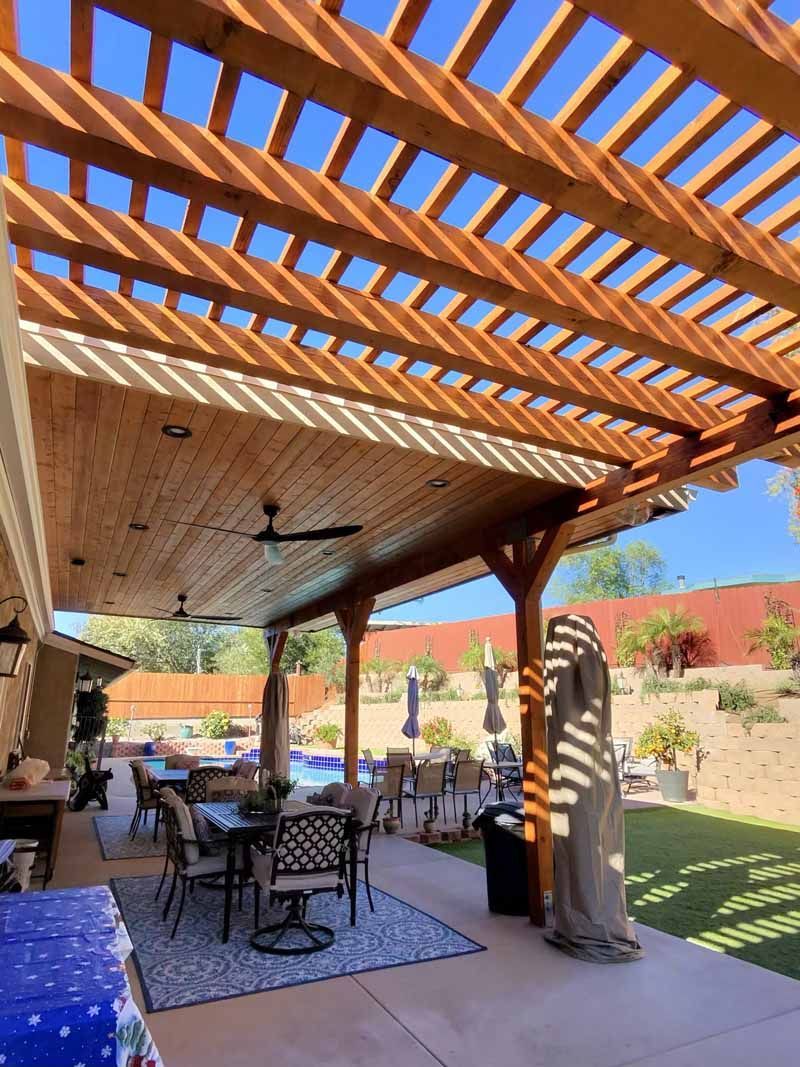 Outdoor patio with wicker seating under a wooden pergola, with patterned shade and a desert landscape beyond.