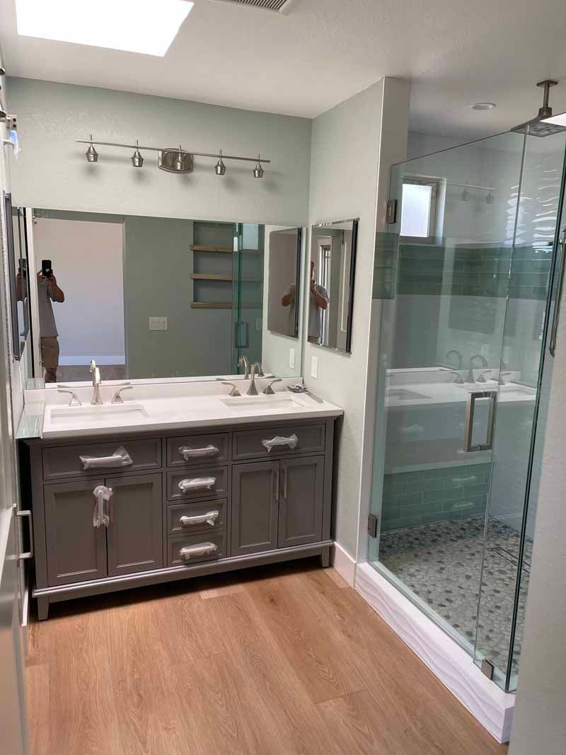 Modern bathroom with gray vanity, double sinks, large mirror, and glass-enclosed shower.