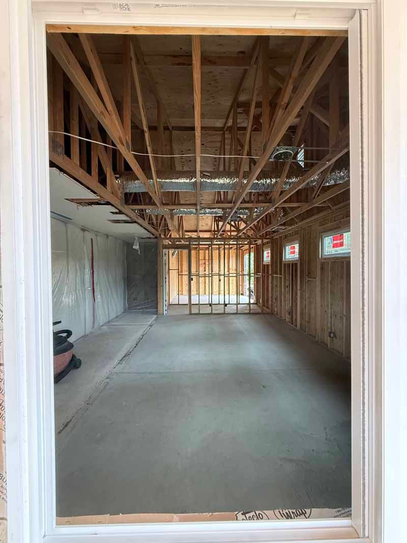 Empty unfinished room with exposed wooden ceiling joists, concrete floor, and window openings.
