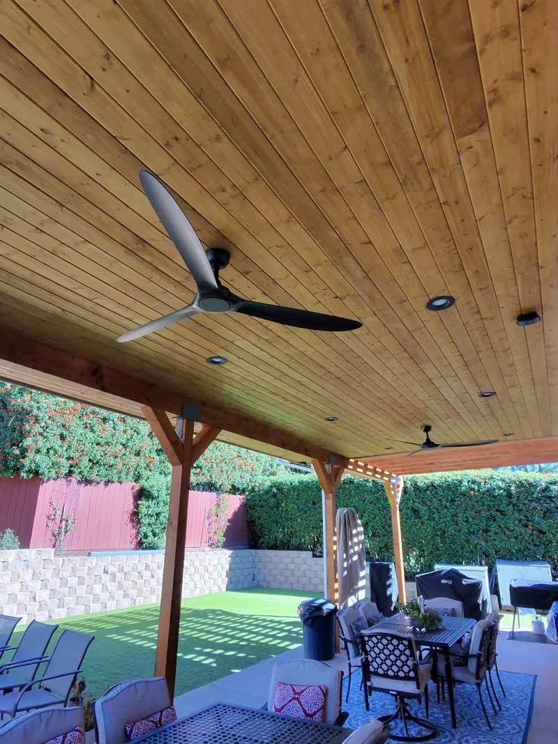 Covered patio with wooden ceiling, ceiling fans, dining table, and a green backyard view