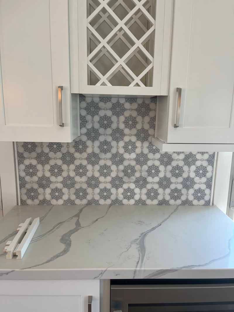 White kitchen counter with marble-look top, patterned backsplash, and white cabinets with a wine rack above