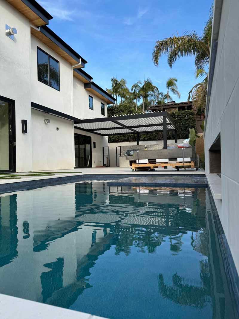 Modern courtyard pool beside white townhomes with palm trees and lounge chairs