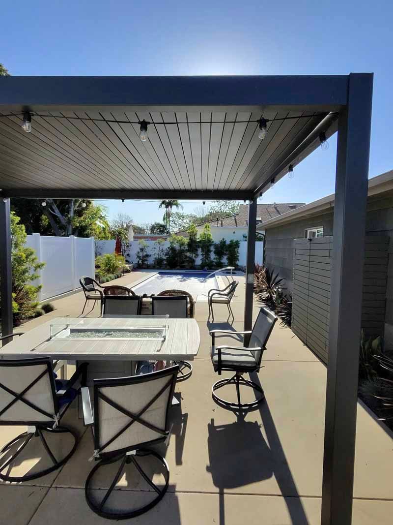 Outdoor patio with pergola, dining table, chairs, and lounge seating in bright sunlight.