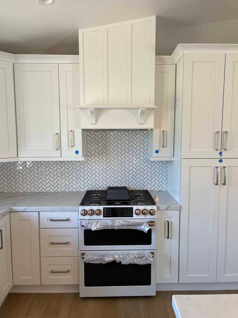 Modern white kitchen with mosaic backsplash and stainless-steel stove centered between cabinets.