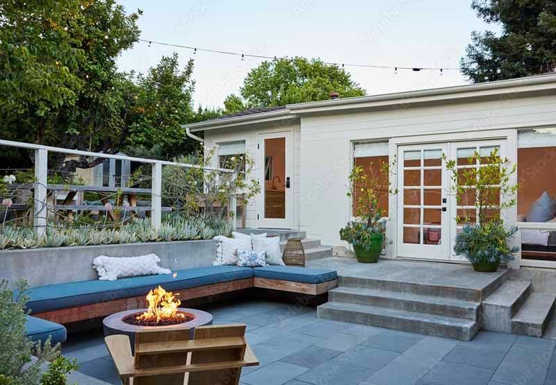 Modern backyard patio with fire pit, built-in seating, steps, and white house exterior at dusk