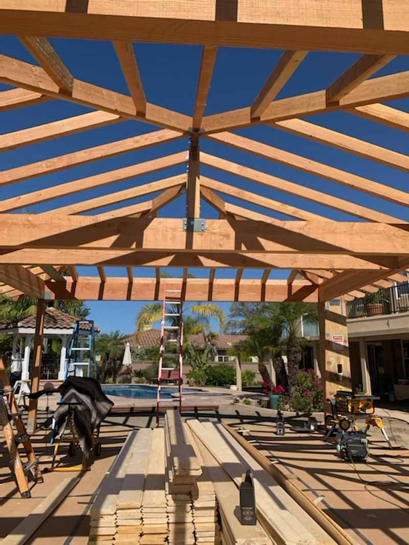 Outdoor patio with wooden pergola, long picnic tables, and a ladder centered in the background.