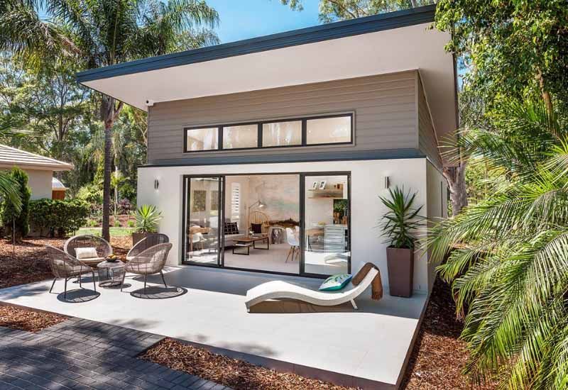 Modern patio with sliding glass doors, lounge chairs, and a shaded tropical backyard.
