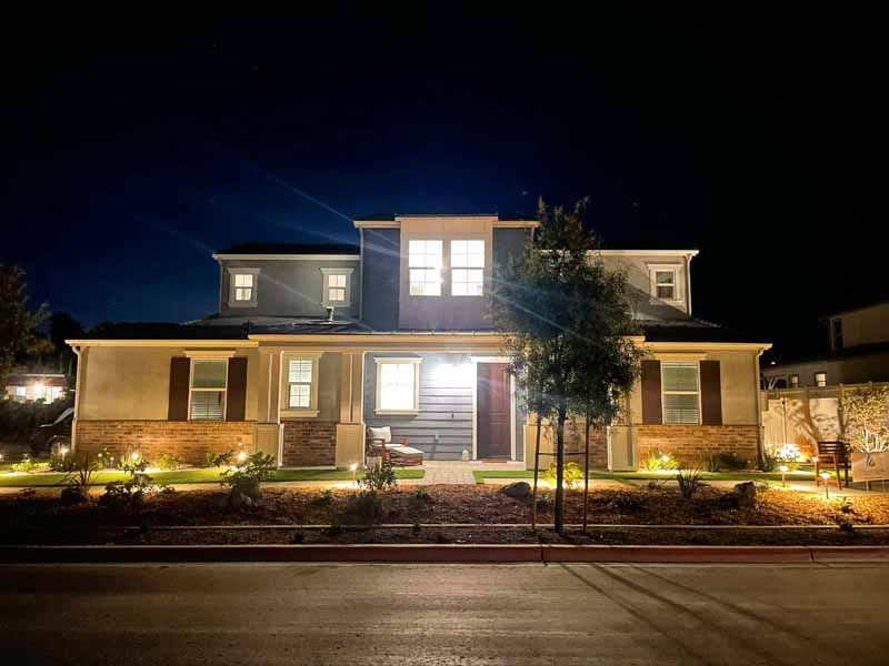 Well-lit two-story house at night with illuminated windows and front landscaping