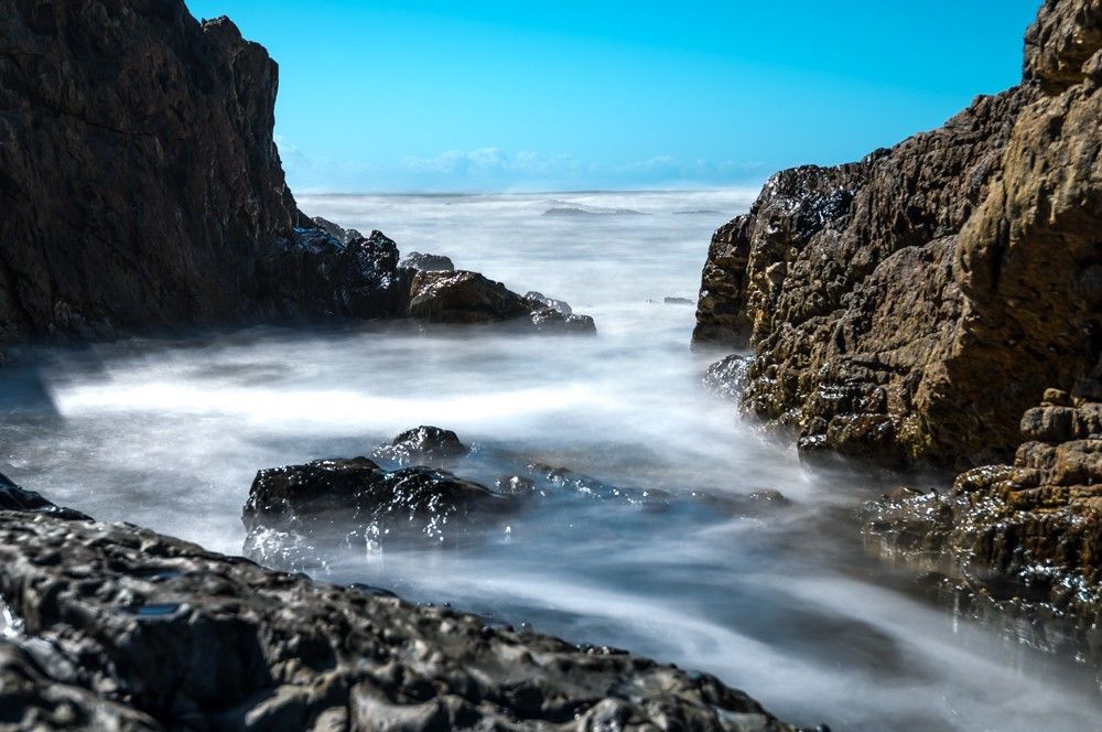 A long exposure photo of waves crashing against rocks on a beach.