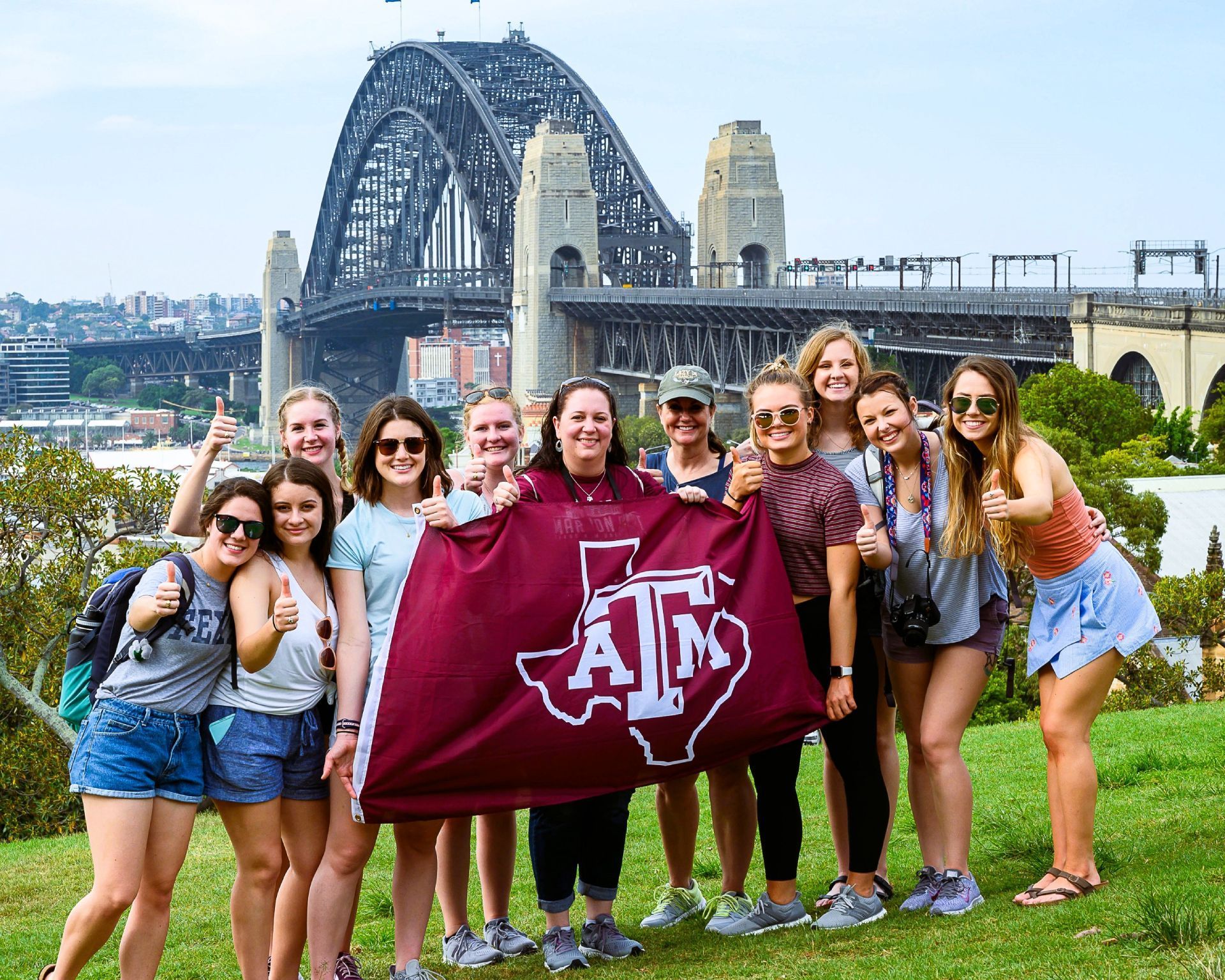 A group of young women are posing for a picture in front of a bridge.