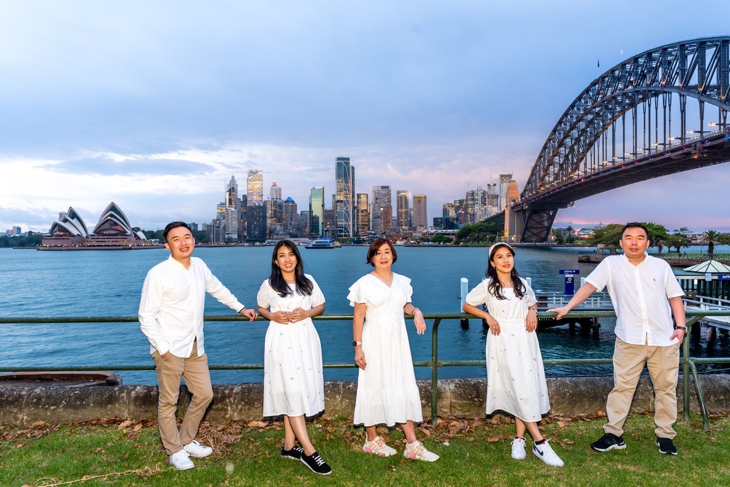 Family posing with Sydney Harbour skyline and bridge. They wear white outfits and stand near the water.