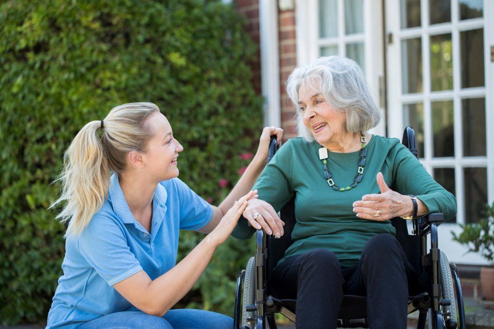 Carer Pushing Senior Woman In Wheelchair Outside Home — iCan Support Services Kawana QLD