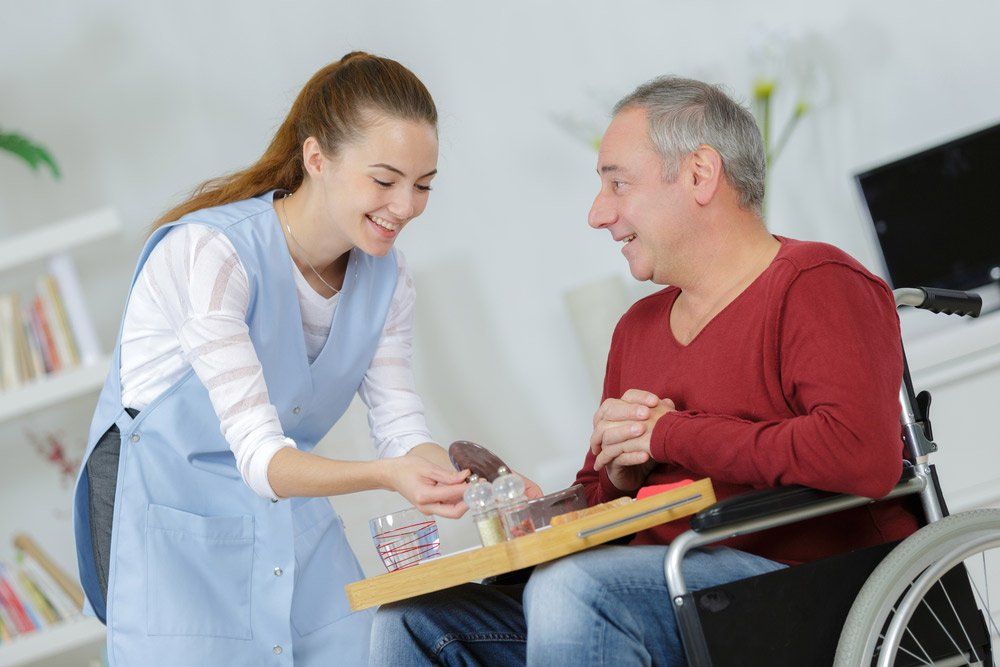Carer Serving Meal To Man In Wheelchair At Home — iCan Support Services Kawana QLD