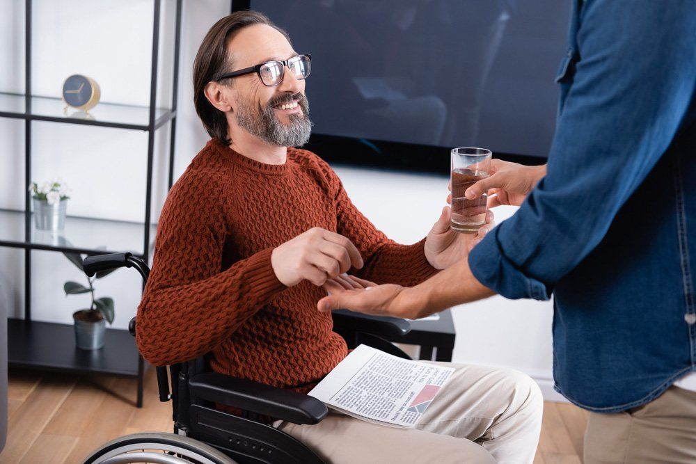 A Man in a Wheelchair is Getting a Glass of Water From Another Man — Queensland Disability Association in Kawana, QLD