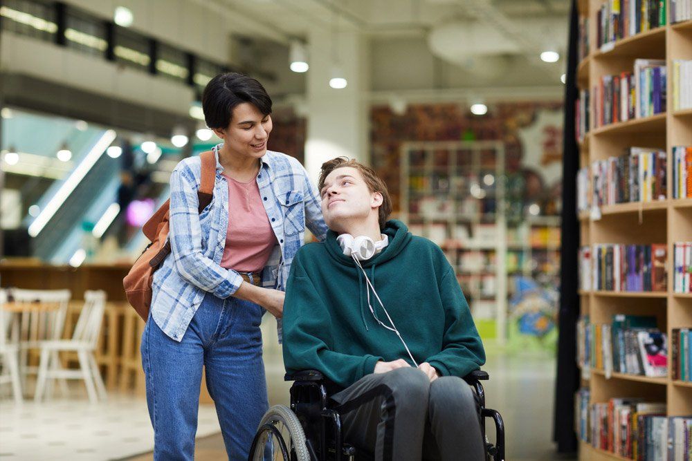 Woman With Satchel Pushing Wheelchair And Talking To Disabled Student — iCan Support Services Kawana QLD