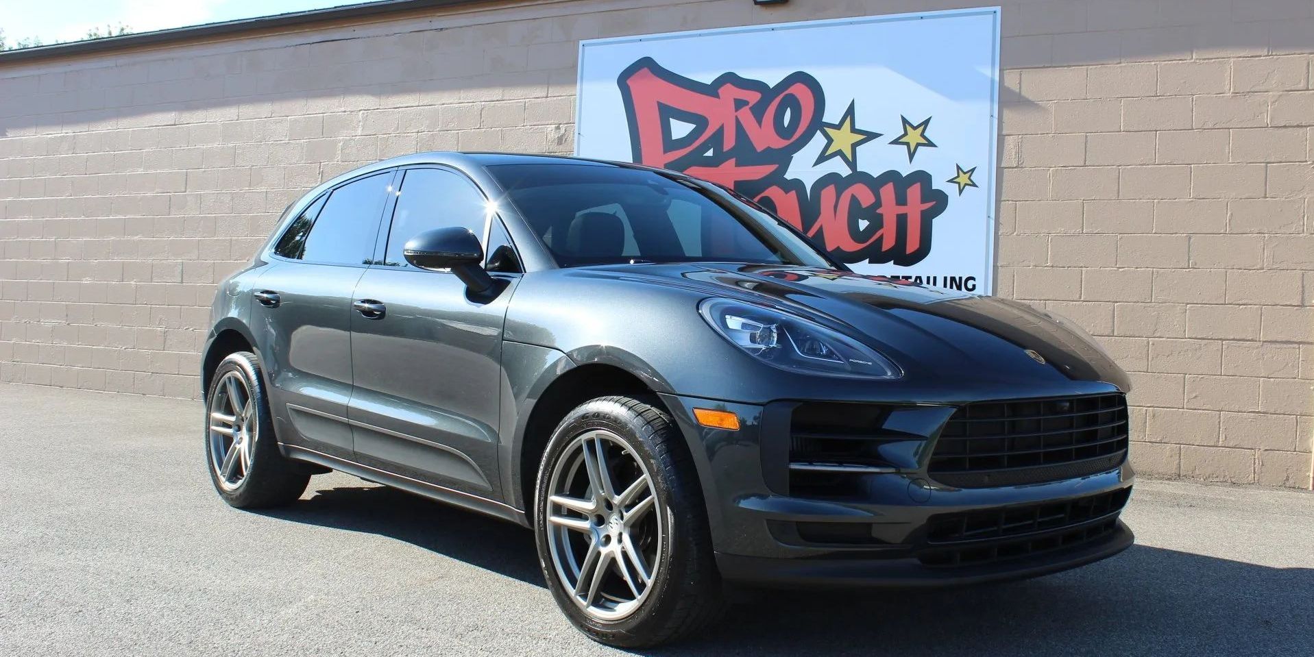 Gray Porsche SUV parked in front of a building with graffiti-style sign.