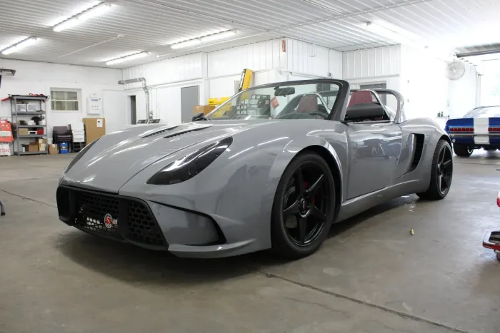 Grey sports car parked in a garage with red interior and black wheels.