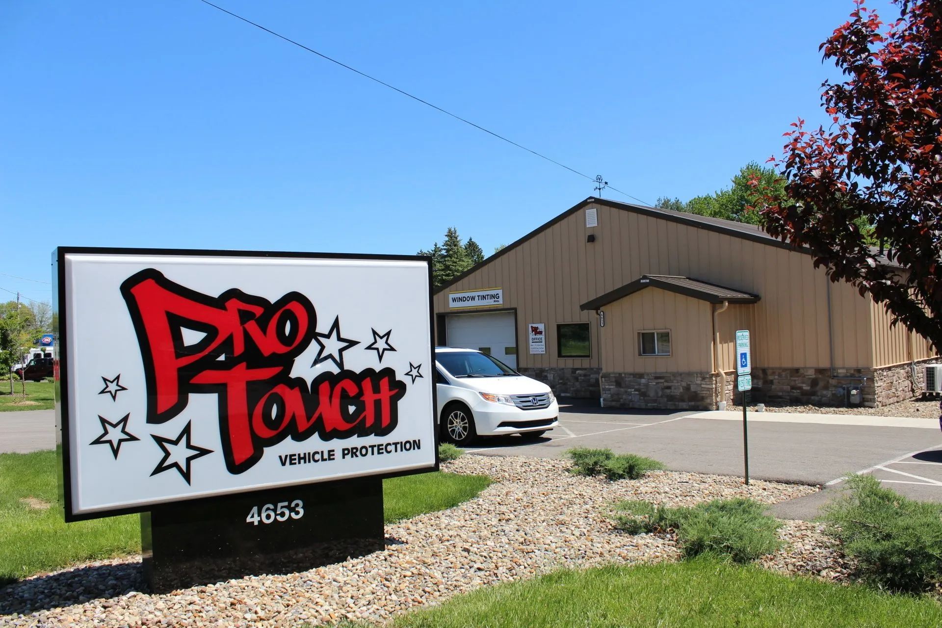 Sign for Pro Touch car wash with building, white car, and blue sky.