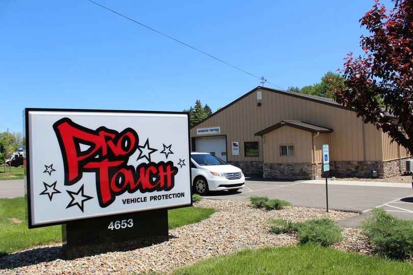 Sign for Pro Touch car wash with building, white car, and blue sky.