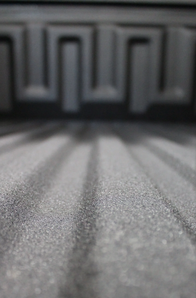 Close-up view of a truck bed with ribbed floor and textured back wall, gray.