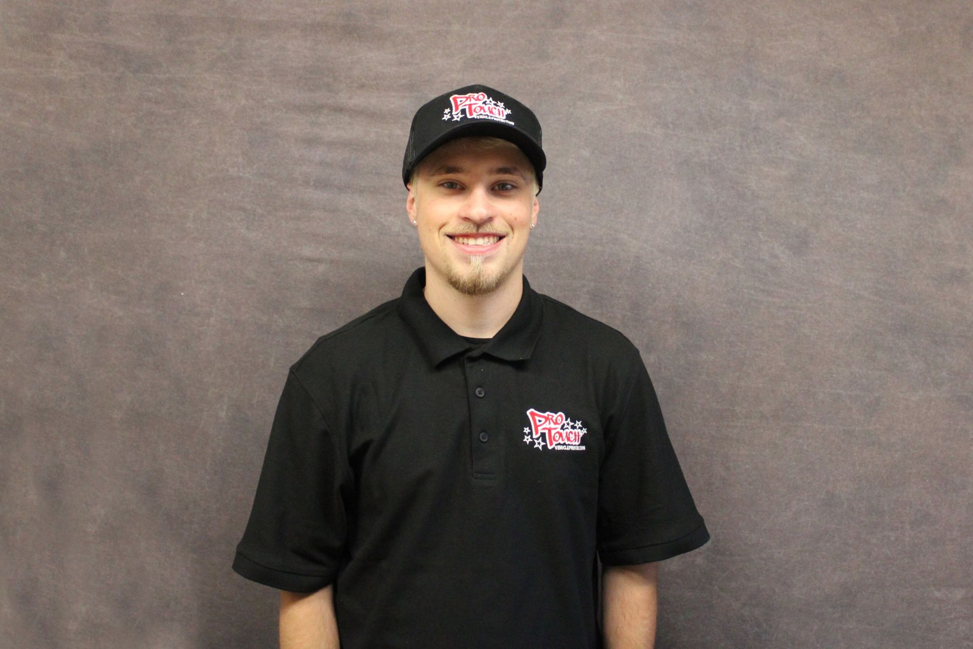 Man in a black shirt and hat smiling at the camera against a gray backdrop.