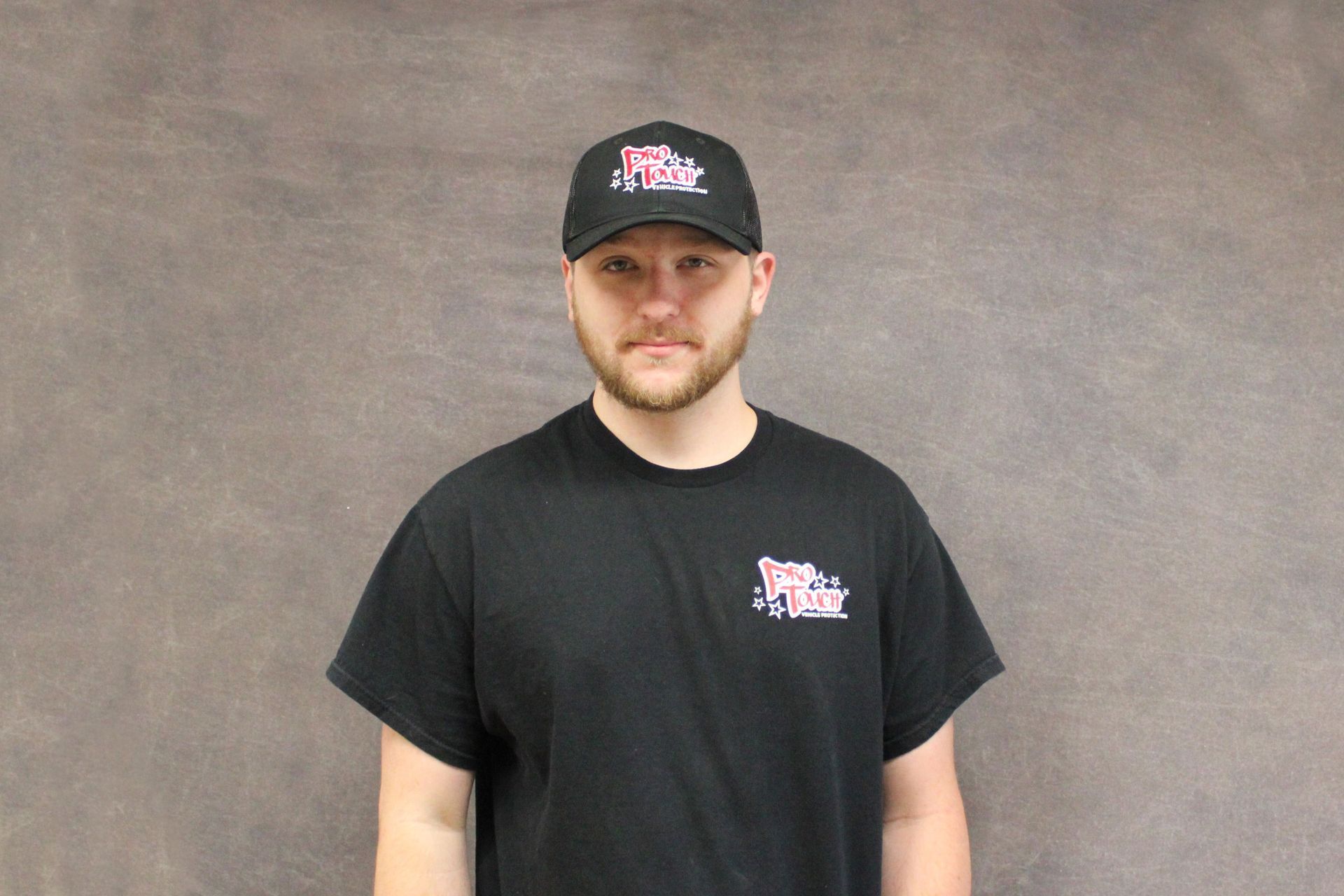 Man in black shirt and hat poses in front of a gray backdrop.