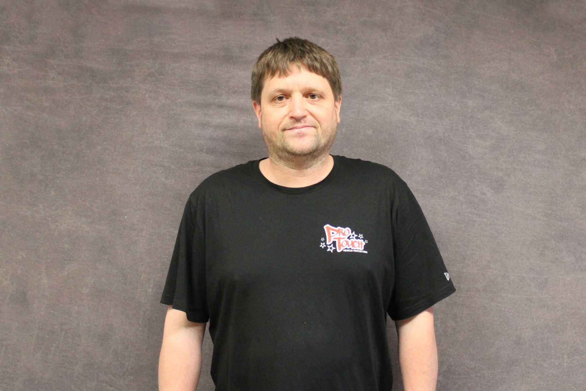 Man in black t-shirt smiles in front of a gray backdrop.