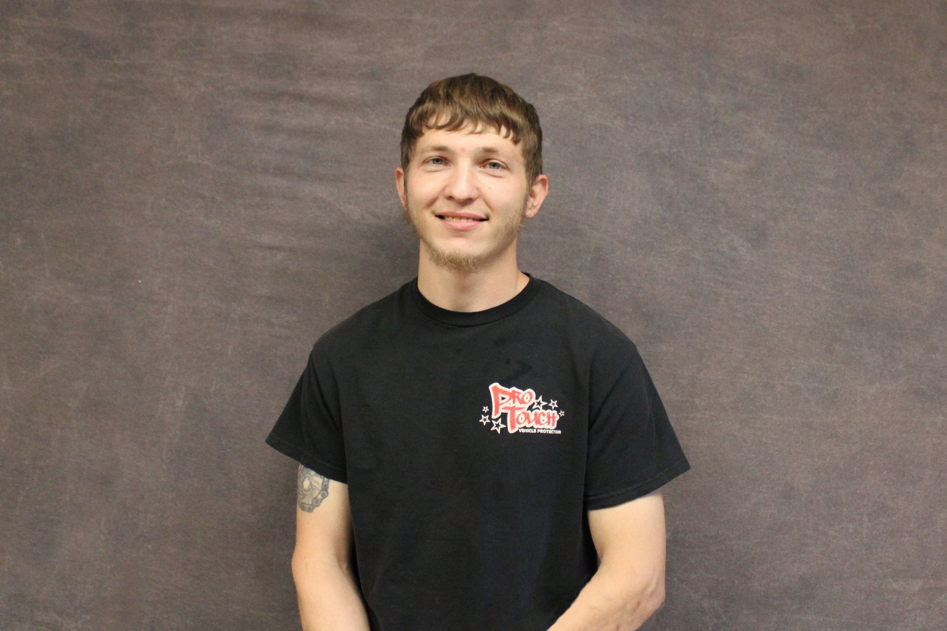 Smiling person in a black shirt stands in front of a gray backdrop.