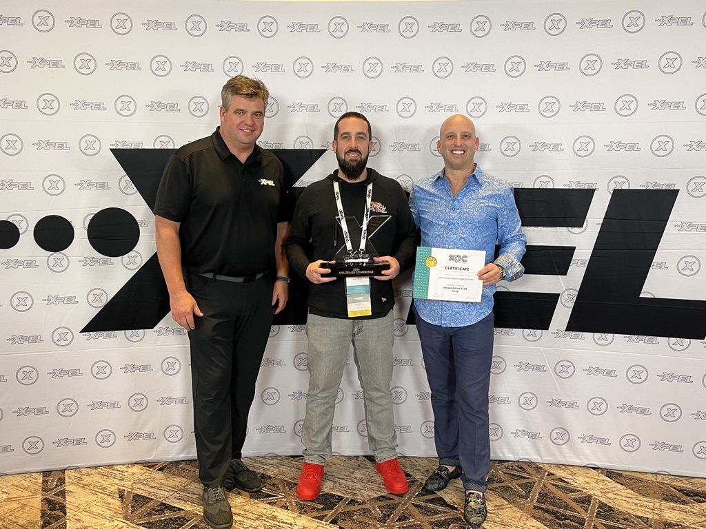 Three men posing for a photo in front of a backdrop, one holding an award and certificate.
