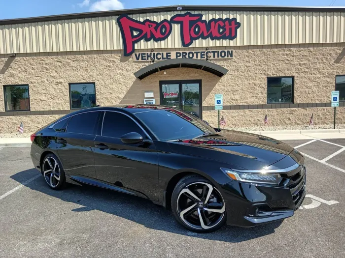 Black sedan parked in front of Pro Touch Vehicle Protection shop. Tinted windows, reflective wheels, gray building.