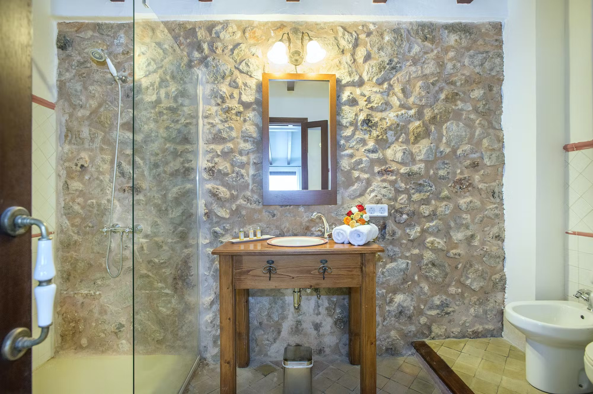 Bathroom with stone wall, wooden vanity, mirror, and toilet.