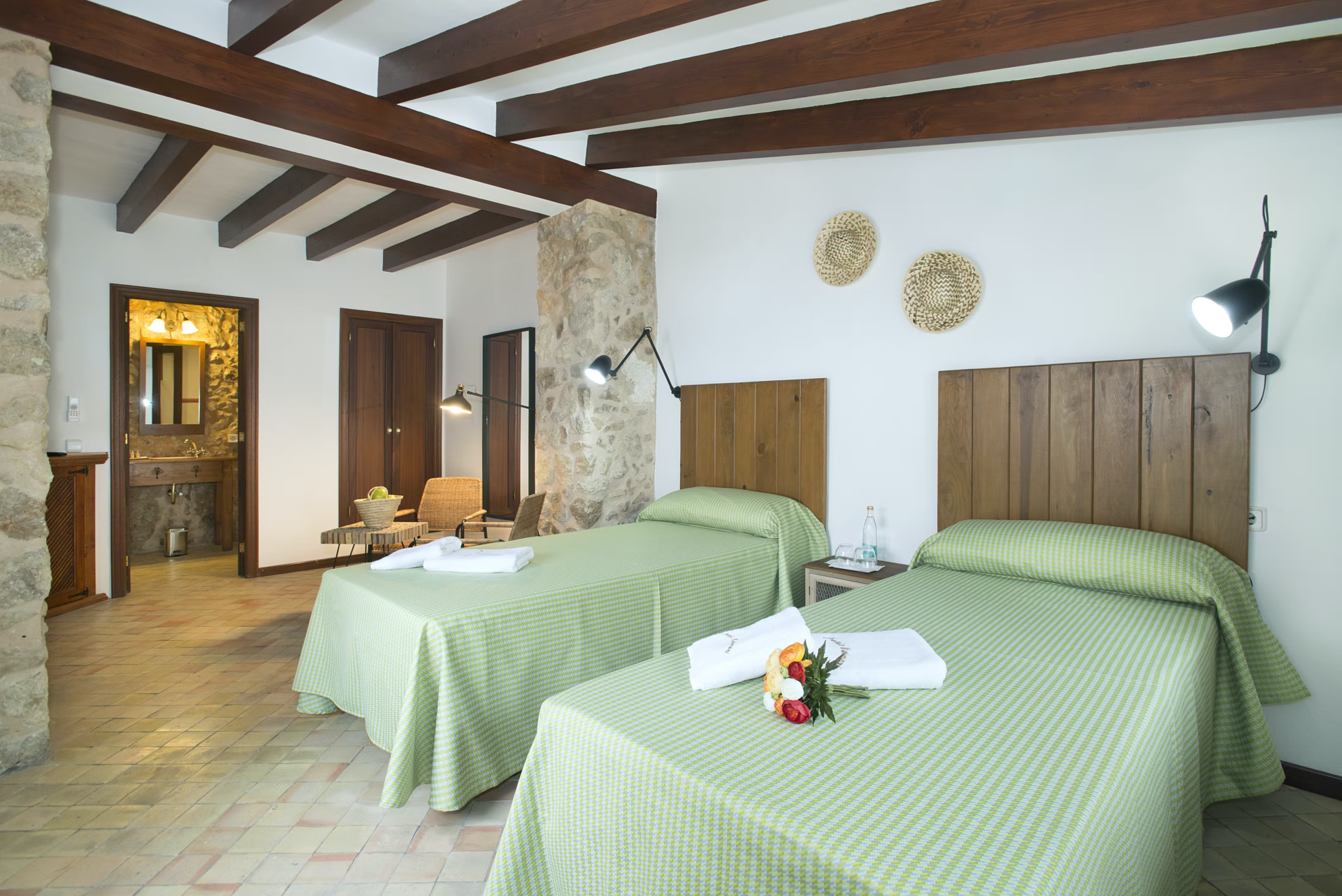 Two twin beds in a rustic room with stone walls, wooden beams, and green bedding.