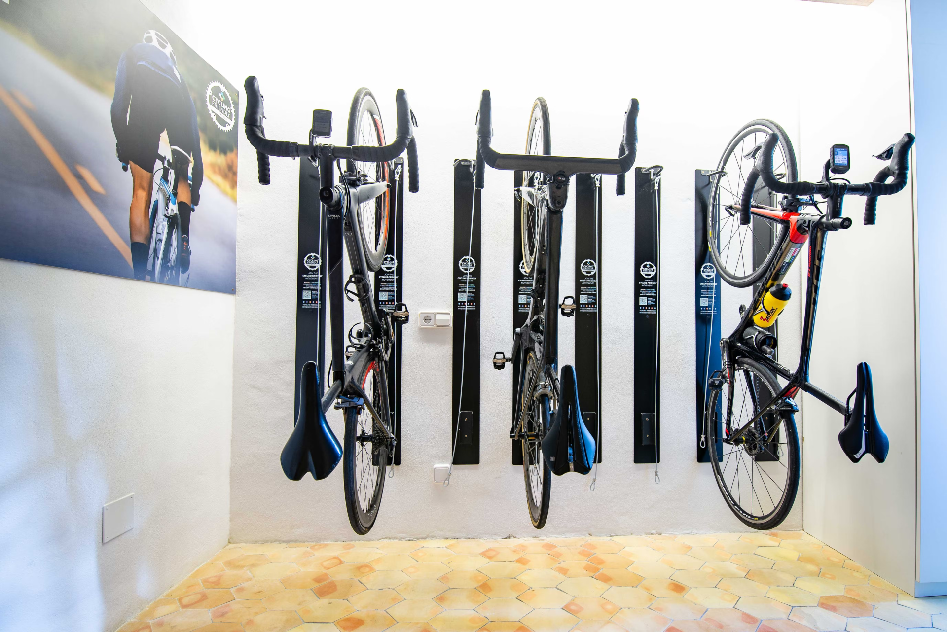 Bikes mounted on black racks on a white wall, next to a promotional poster.