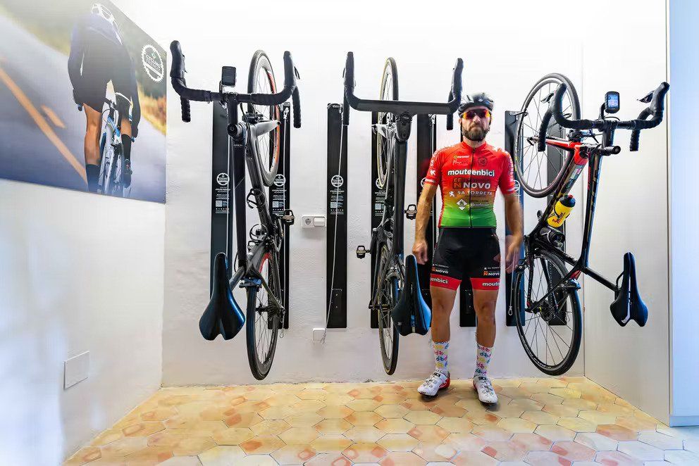 Cyclist in red jersey stands before wall-mounted bike racks holding three bikes.