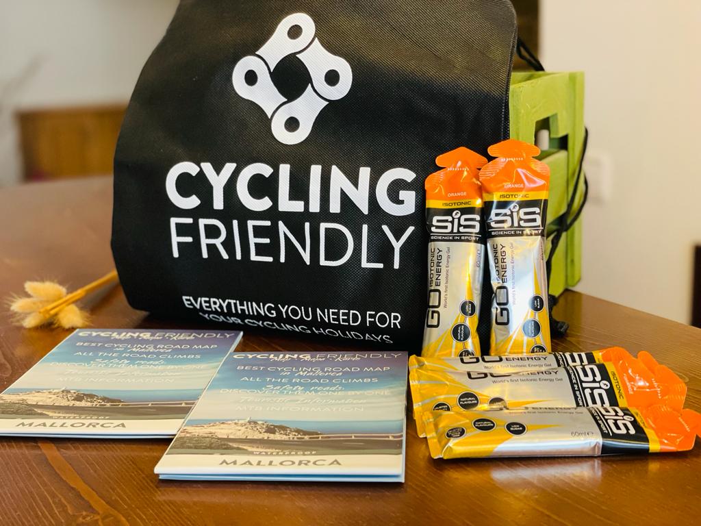 Cycling-themed gift bag with energy gels, bars, gloves, and brochures on a wooden table.