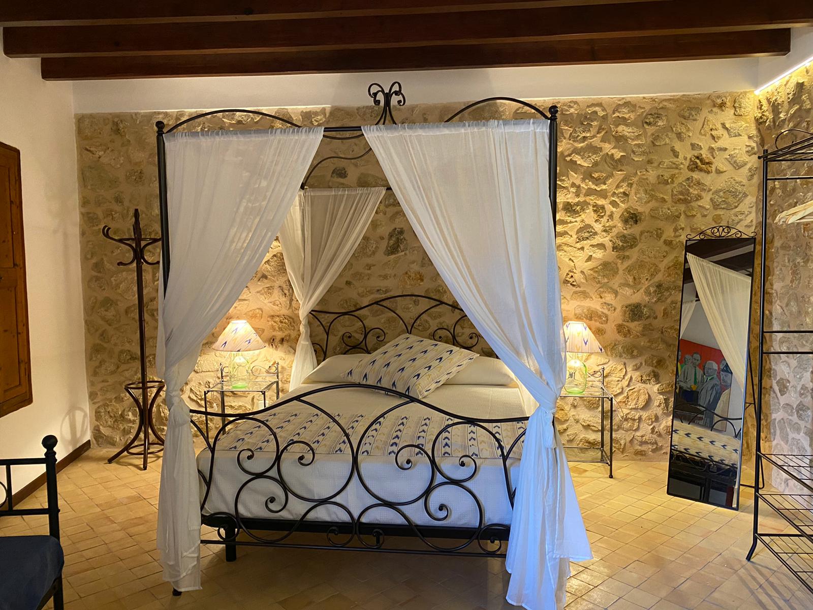 Four-poster bed in a bedroom with stone walls, two nightstands, and a decorative mirror.