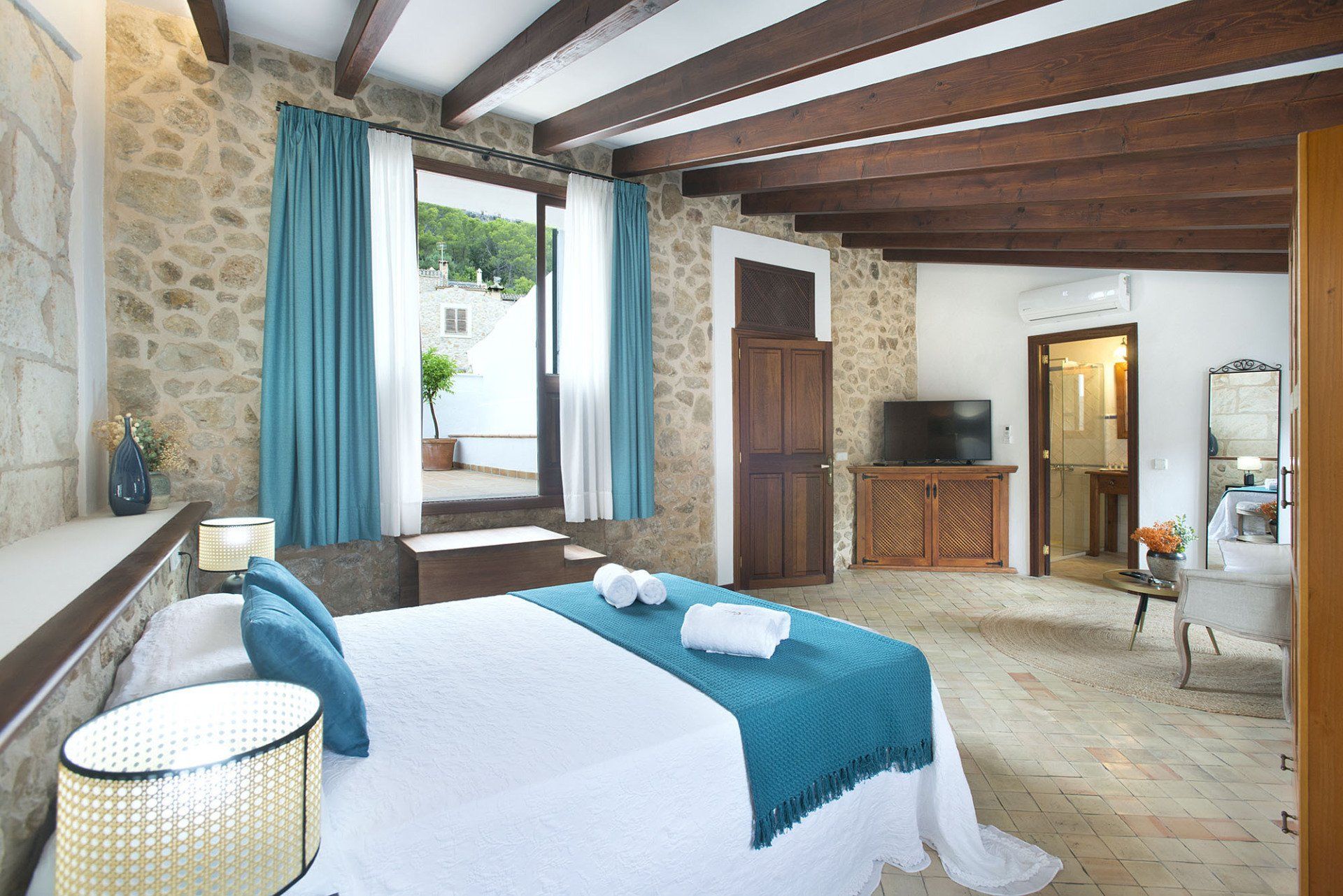 Bedroom with stone walls, wooden beams, turquoise accents, and a doorway to a patio.