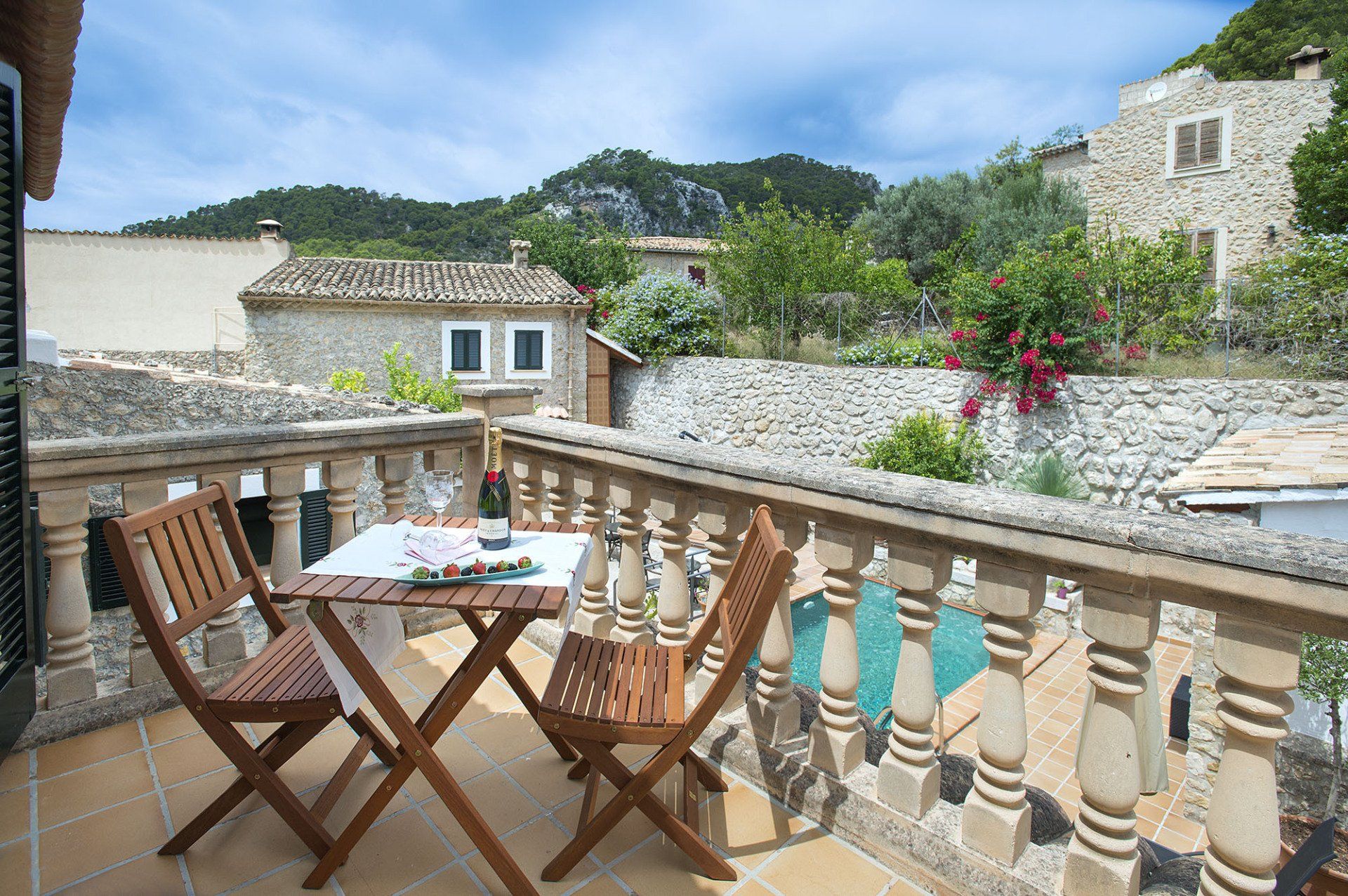 Balcony with table and chairs overlooking a stone village and mountains.