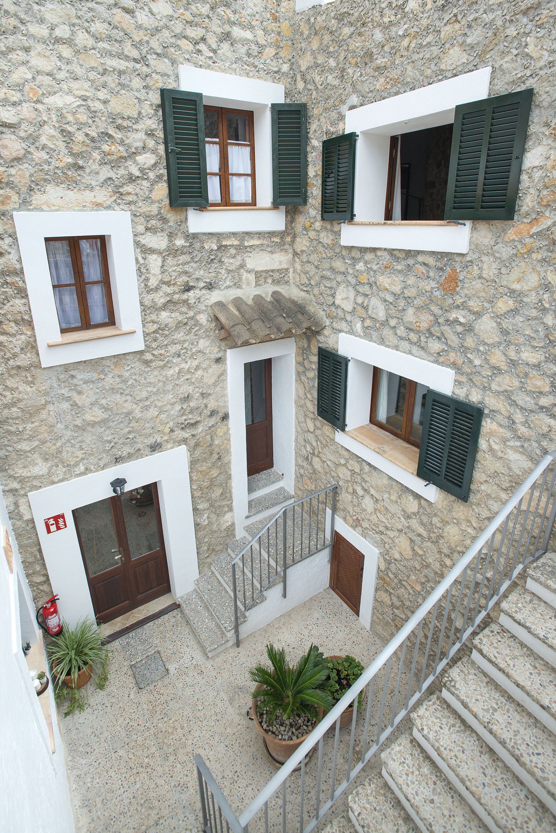 Stone building facade with multiple windows and door, some with green shutters, exterior stairs.