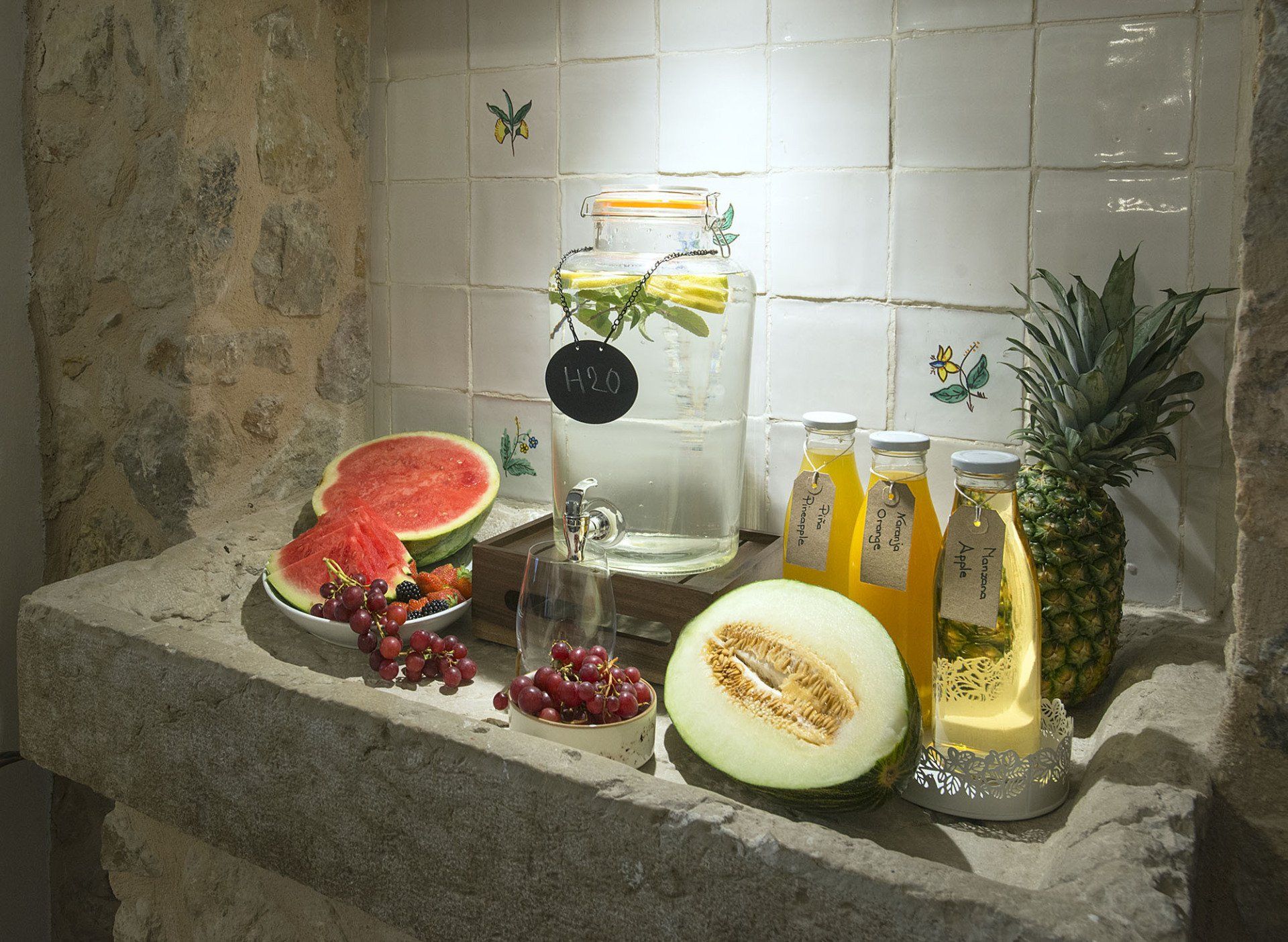 Fruits and drinks on a stone shelf in front of white tiled wall